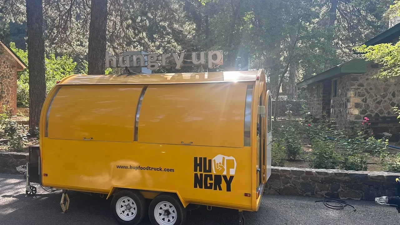 The closed trailer in sunlight showing the HUNGRY logo and www.hupfoodtruck.com painted on the yellow body.